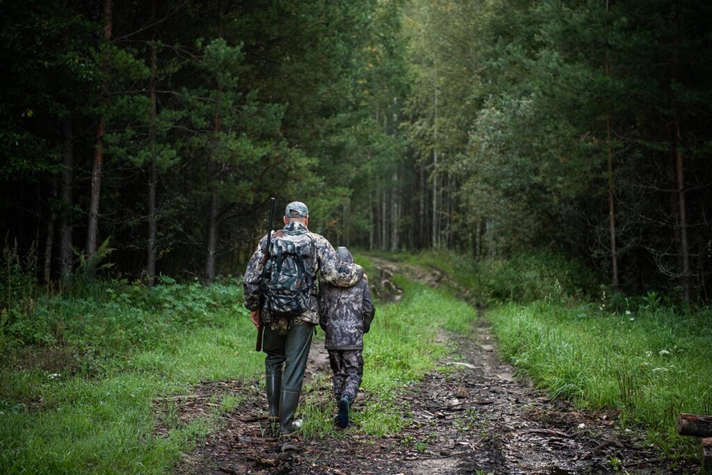 Father and son hunters going away through rural forest